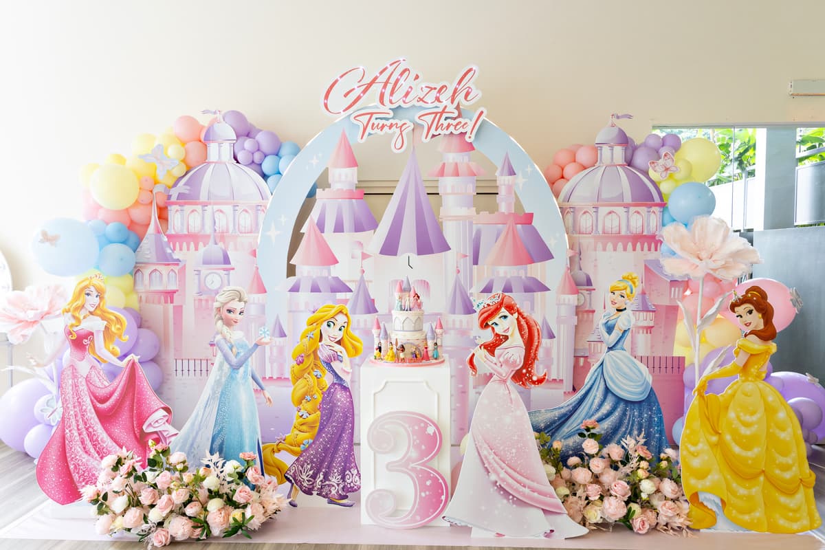 Disney Princess-themed 3rd birthday backdrop with castle cutout, princess standees, and pastel balloon garlands