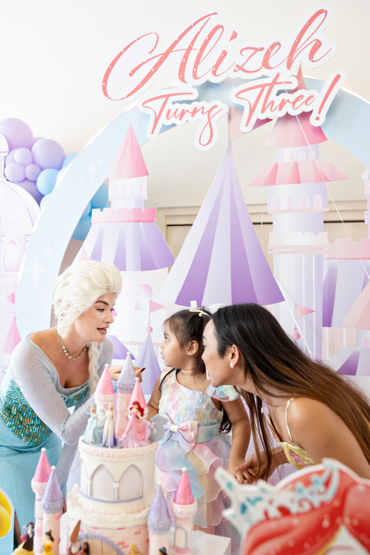 Birthday girl blowing out candles with Elsa character performer and mom