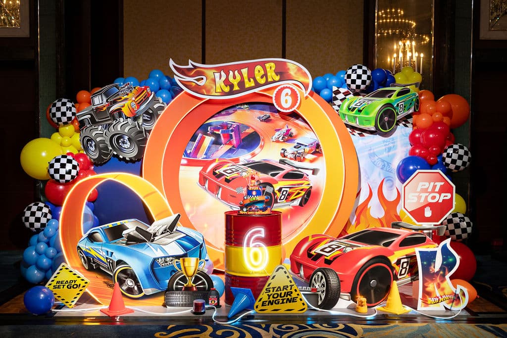 Hot Wheels backdrop with race car standees and balloon garlands in primary colours